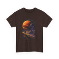 A dark brown short-sleeve crewneck t-shirt featuring a large, colorful cosmic graphic print on the front, showing a figure looking at planets in space.