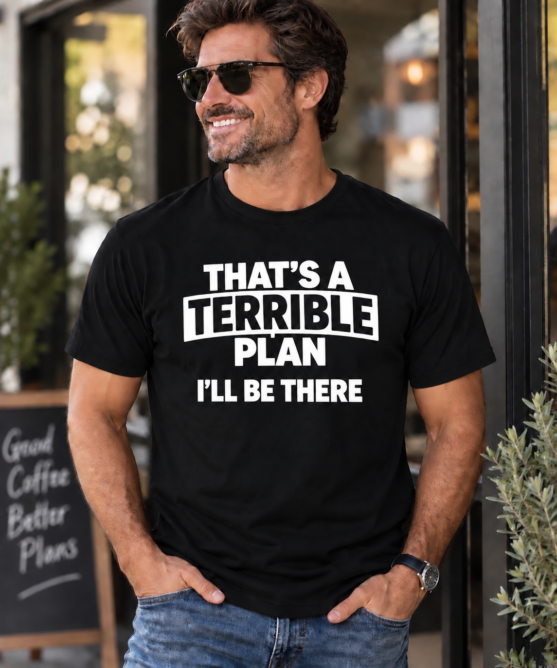 A man wearing a black graphic t-shirt with the white printed text 'THAT'S A TERRIBLE PLAN I'LL BE THERE', standing in front of a storefront.