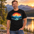 This classic black cotton T-shirt features a vivid sunset landscape with snowcapped peaks, towering evergreens, reflective blue water, and two paddlers enjoying the stillness of the lake.