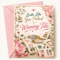 A mahjong themed engagement greeting card with a pink envelope behind it. The card features the phrase 'Looks Like You Picked a Winning Tile' in decorative script over an illustration of mahjong tiles, including a central ring and diamond motif, with pink flowers and gold border details.