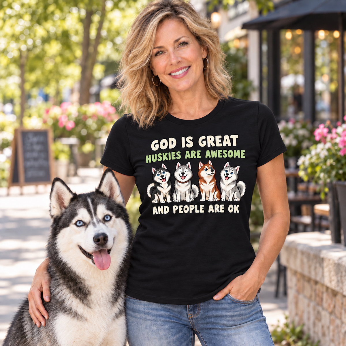 A woman wearing a black graphic t-shirt with a humorous husky slogan and illustrations of four huskies, standing outdoors next to a husky dog.