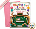 A Mahjong-themed greeting card with a pink envelope behind it, featuring colorful text reading 'Wishing You Luck On Your Journey' and an illustrated mahjong table scene. A pink ribbon in the corner reads 'MahjongFun', and a round badge says 'As seen on'.