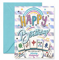 A birthday greeting card with a matching light blue envelope. The card features a white and iridescent holographic striped background with a rainbow, colorful 'HAPPY Birthday' text, mahjong tile graphics, and dice.