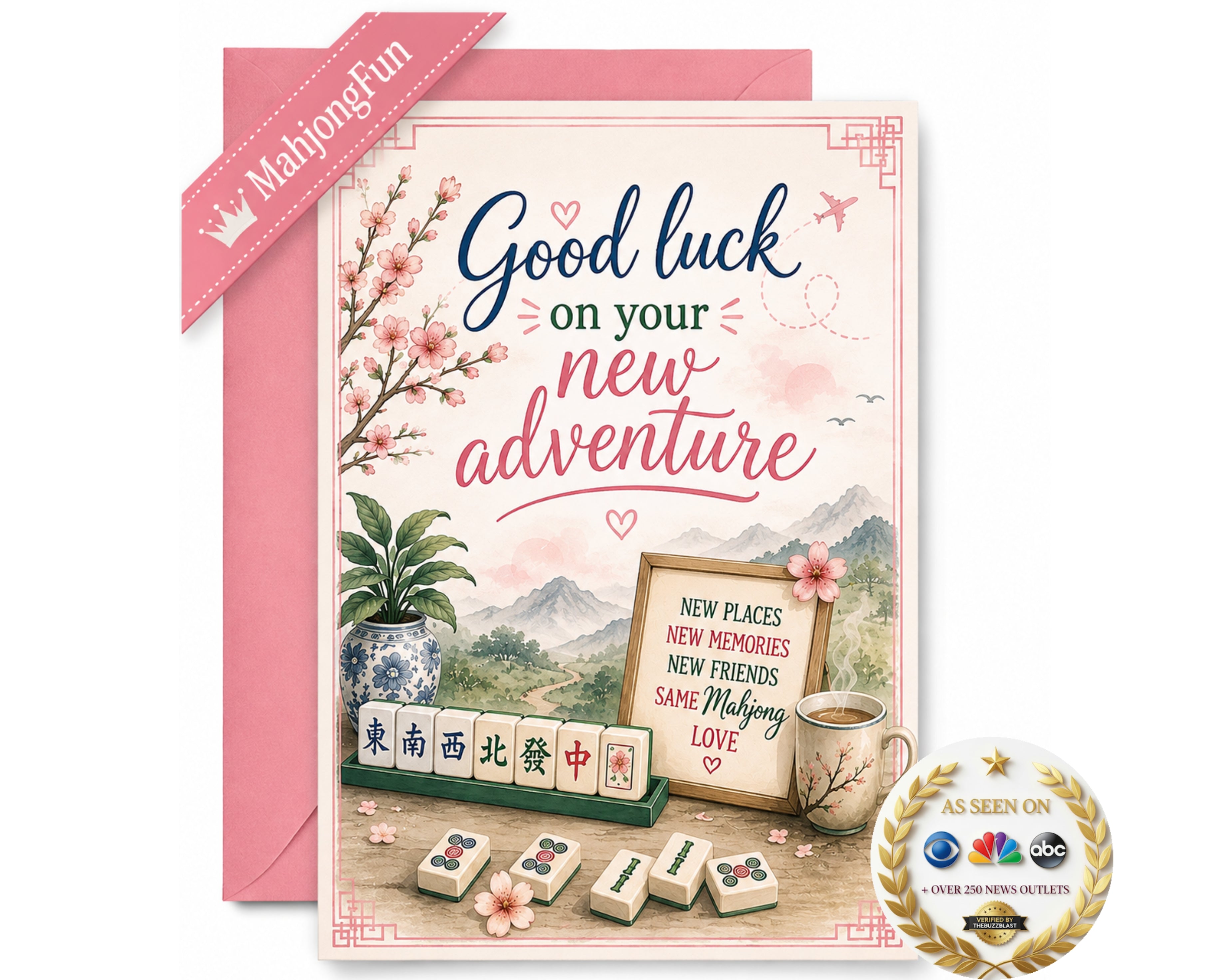 A pink and white 'Good luck on your new adventure' greeting card with a matching pink envelope. The card features Chinese-themed illustrations including mahjong tiles, a potted plant, a cup of tea, and a scenic mountain background.