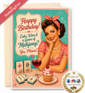 A birthday greeting card featuring a retro 1950s-style illustration of a woman with a pink polka-dot headband and pink dress, seated at a table with mahjong tiles, a glass of red wine, and a cupcake. The card reads, 'Happy Birthday! Cake, Wine & a Game of Mahjong? Yes, Please!' A kraft envelope is partially visible behind the card, with a pink 'MahjongFun' ribbon and a circular 'As Seen On' badge in the corners.