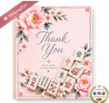 A square pink card or gift box design featuring floral illustrations and several Mahjong tiles arranged around the text 'Thank You' and 'WITH DEEP APPRECIATION.' A pink ribbon in the top-left corner reads 'MahjongFun,' and a gold 'Seen on' badge appears at the bottom-right.