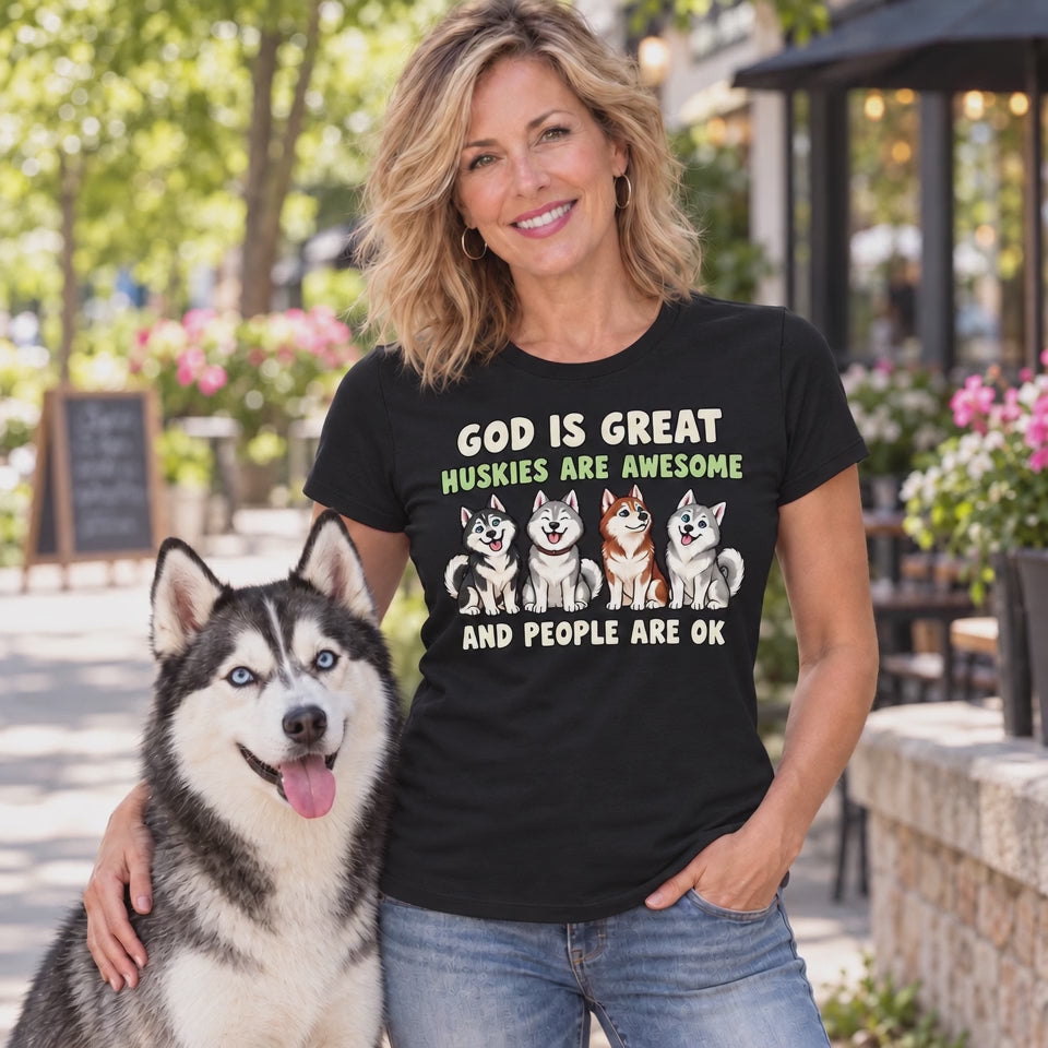 A Video of a woman wearing a black graphic t-shirt with a humorous husky slogan and illustrations of four huskies, standing outdoors next to a husky dog.